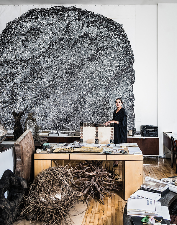 Oka Doner poses in her studio, in front of her enormous ink drawing inspired by a photograph of mother-of-pearl—in which each line traces the activity of a mollusk laying down its nacre. | SASHA MASLOV PHOTO